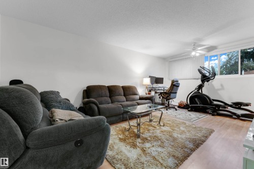 Living area with light wood-finish flooring, white walls, and a white ceiling fan - #104 11445 41 Av Nw, Edmonton, AB - Indoor Photo Showing Living Room