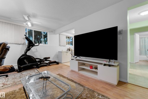 Spacious lower-level room featuring wood-finish flooring, white walls, and built-in lighting - #104 11445 41 Av Nw, Edmonton, AB - Indoor Photo Showing Gym Room