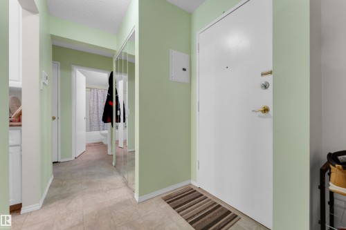 Entryway featuring a white solid door with brass hardware, light green walls, wood-finish flooring, and a mirrored closet door - #104 11445 41 Av Nw, Edmonton, AB - Indoor Photo Showing Other Room