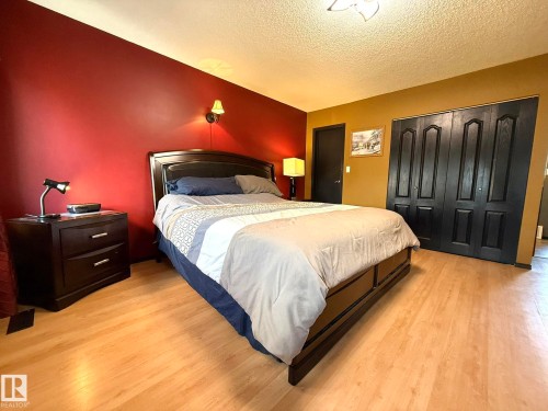 Spacious room featuring light wood-finish flooring, a wall-mounted sconce, and dark paneled bi-fold closet doors - 4508 57 Avenue, Lamont, AB - Indoor Photo Showing Bedroom