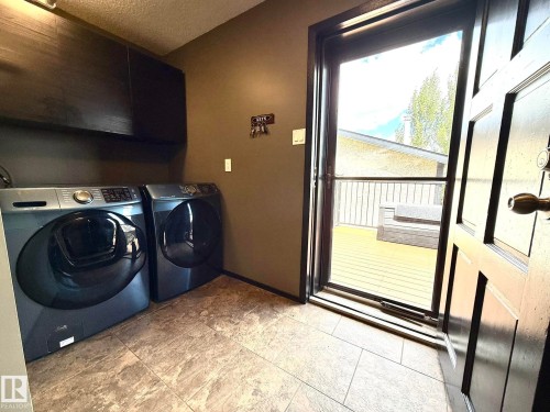 Laundry area featuring tiled flooring, dark wall-mounted cabinetry, and direct exterior access to a wood deck - 4508 57 Avenue, Lamont, AB - Indoor Photo Showing Laundry Room