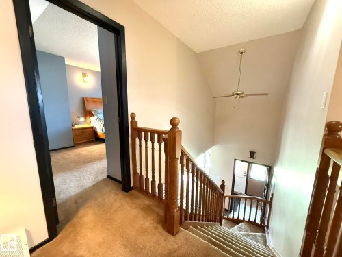 Carpeted staircase with wooden banister, featuring a vaulted ceiling and overhead fan - 4508 57 Avenue, Lamont, AB - Indoor Photo Showing Other Room