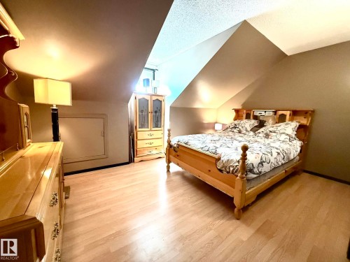 Bedroom featuring a sloped ceiling, wood-finish flooring, and a small, built-in window - 4508 57 Avenue, Lamont, AB - Indoor Photo Showing Bedroom