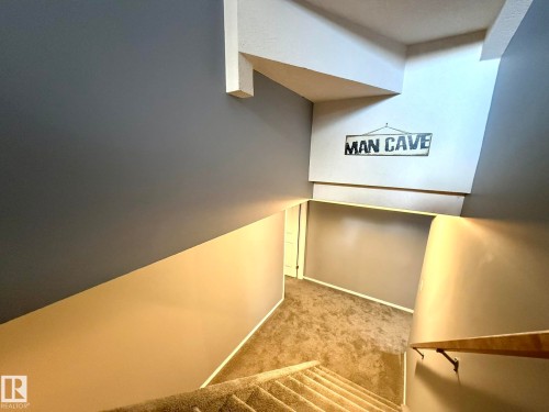 Carpeted staircase with a wood-finish handrail descending to a lower level with carpeted flooring - 4508 57 Avenue, Lamont, AB - Indoor Photo Showing Other Room