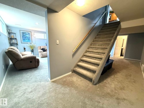 Carpeted staircase with a wood handrail, opening to a carpeted recreation area - 4508 57 Avenue, Lamont, AB - Indoor Photo Showing Other Room