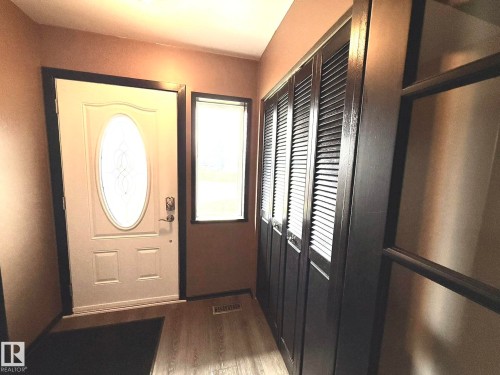 Entryway featuring a white door with decorative oval glass insert, wood-finish flooring, and a window with blinds - 4508 57 Avenue, Lamont, AB - Indoor Photo Showing Other Room