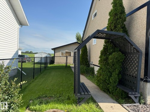 Side yard featuring a concrete path, decorative black pergola with built-in seating, and a privacy fence - 4508 57 Avenue, Lamont, AB - Outdoor With Exterior