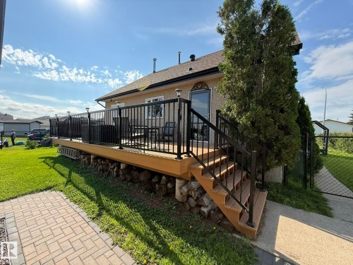 Rear exterior featuring an elevated deck with black metal railings, a full staircase, and a stucco finish on the home - 4508 57 Avenue, Lamont, AB - Outdoor With Deck Patio Veranda