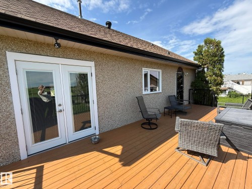 Expansive deck featuring wood-finish flooring, white-framed double glass doors, a window, and stucco-style exterior siding - 4508 57 Avenue, Lamont, AB - Outdoor With Deck Patio Veranda With Exterior
