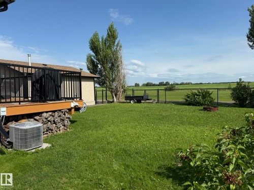 Expansive green lawn featuring a perimeter fence and a visible fire pit - 4508 57 Avenue, Lamont, AB - Outdoor With Deck Patio Veranda