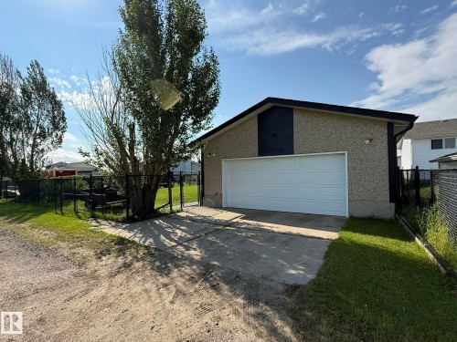 Detached garage with a white overhead door, textured stucco exterior, and black trim - 4508 57 Avenue, Lamont, AB - Outdoor