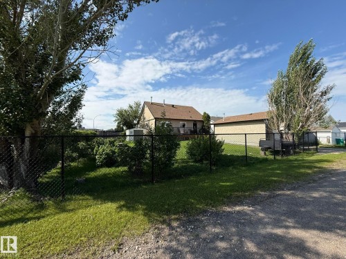 Chain link fence enclosing a grassy area with mature trees and established shrubbery - 4508 57 Avenue, Lamont, AB - Outdoor