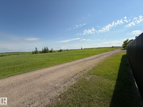 Expansive green field with a gravel road and a dark corrugated fence - 4508 57 Avenue, Lamont, AB - Outdoor With View