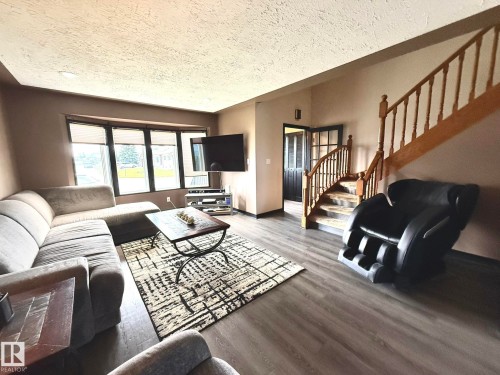 Spacious living area featuring wood-finish flooring and a curved staircase with wood banisters - 4508 57 Avenue, Lamont, AB - Indoor Photo Showing Living Room