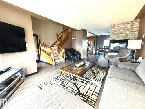 Open-concept living area featuring light wood-finish flooring, a stacked stone fireplace with an integrated hearth, and a wooden staircase with balusters - 4508 57 Avenue, Lamont, AB - Indoor Photo Showing Living Room