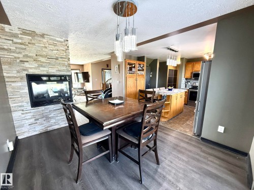 Open-concept dining area featuring a stacked stone fireplace with an electric insert, wood-finish flooring, and a contemporary chandelier - 4508 57 Avenue, Lamont, AB - Indoor Photo Showing Dining Room With Fireplace