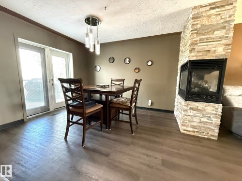 Corner fireplace with stone veneer surround, wood-finish flooring, contemporary pendant lighting, and double glass doors - 4508 57 Avenue, Lamont, AB - Indoor Photo Showing Dining Room With Fireplace