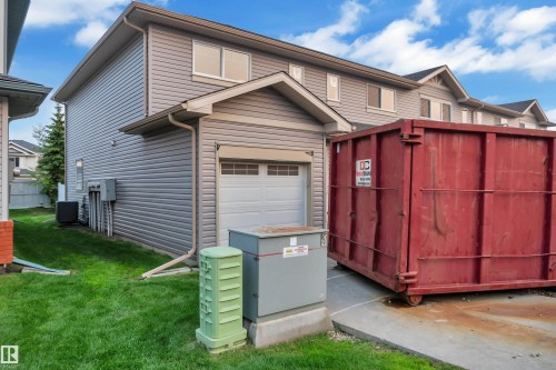 Rear exterior featuring light grey horizontal siding, a single-car garage with a white sectional door, and a concrete driveway - #5 18004 89 St Nw, Edmonton, AB - Outdoor With Exterior