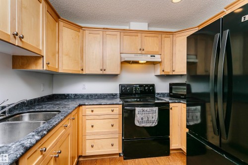 Kitchen featuring light wood cabinetry, stone-look countertops, and a black appliance suite - #106 12110 106 Av Nw, Edmonton, AB - Indoor Photo Showing Kitchen With Double Sink