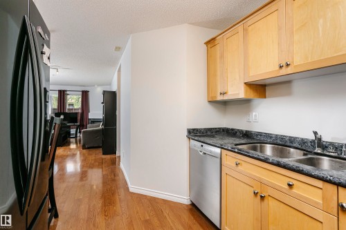 Kitchen featuring wood-finish cabinetry with silver-tone hardware, a stainless steel double basin sink, and a stainless steel dishwasher - #106 12110 106 Av Nw, Edmonton, AB - Indoor Photo Showing Kitchen With Double Sink