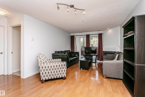 Open-concept living area featuring wood-finish flooring, a built-in fireplace with a tile surround, and a built-in dark wood shelving unit - #106 12110 106 Av Nw, Edmonton, AB - Indoor Photo Showing Living Room