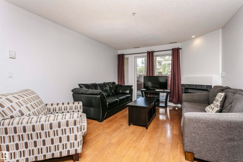 Bright living space featuring wood-finish flooring, a wall-mounted thermostat, and a sliding glass door - #106 12110 106 Av Nw, Edmonton, AB - Indoor Photo Showing Living Room