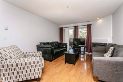 Bright living space featuring wood-finish flooring, a wall-mounted thermostat, and a sliding glass door - 