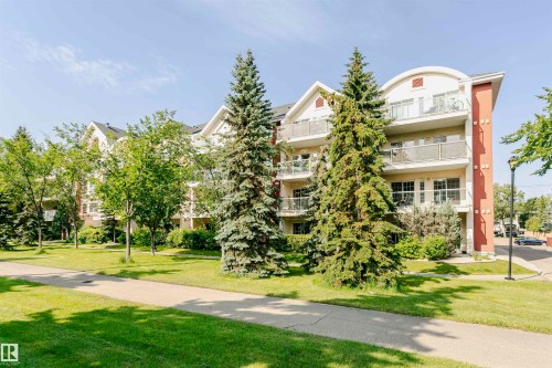 Multi-story residence featuring a combination of stucco and siding facade, multiple balconies with metal railings, gabled rooflines, and mature evergreen and deciduous trees - #106 12110 106 Av Nw, Edmonton, AB - Outdoor