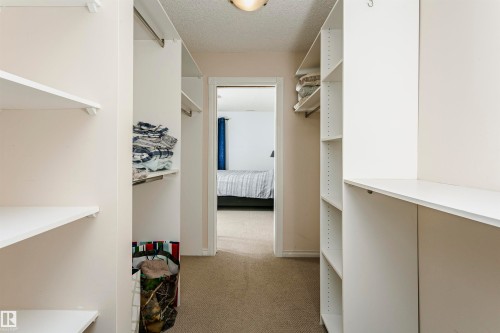 Walk-through closet featuring built-in white shelving, hanging rods, and carpet flooring - #106 12110 106 Av Nw, Edmonton, AB - Indoor