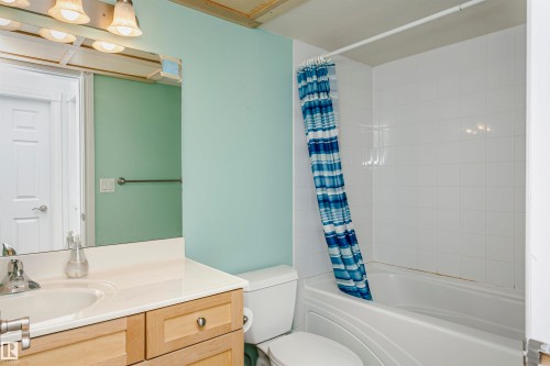 Bathroom featuring a light-toned vanity with an integrated sink, a white toilet, and a bathtub with white tiled surround - #106 12110 106 Av Nw, Edmonton, AB - Indoor Photo Showing Bathroom