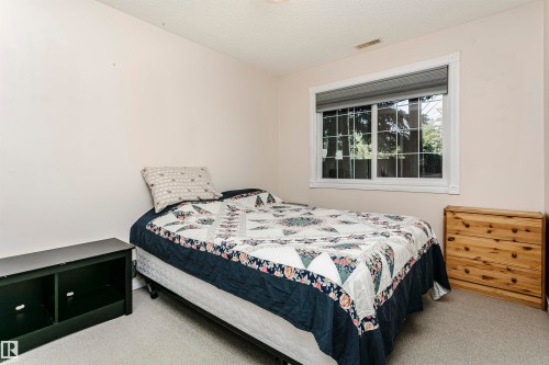 Bedroom with a framed window featuring white grilles and a roller shade, light-toned walls, and neutral carpeting - #106 12110 106 Av Nw, Edmonton, AB - Indoor Photo Showing Bedroom