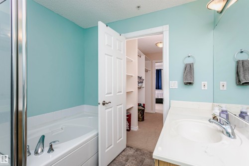 Bathroom featuring a white built-in soaking tub with chrome fixtures, a glass shower enclosure, a vanity with an integrated sink, a large wall mirror, and an adjacent walk-in closet with built-in shelving - #106 12110 106 Av Nw, Edmonton, AB - Indoor Photo Showing Bathroom