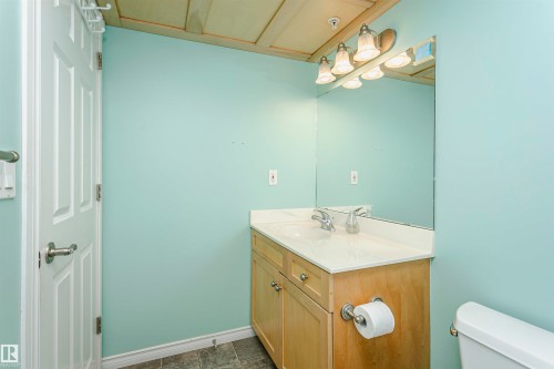 Bathroom featuring a light wood-finish vanity with a single basin sink, mounted mirror, and vanity lighting - #106 12110 106 Av Nw, Edmonton, AB - Indoor Photo Showing Bathroom
