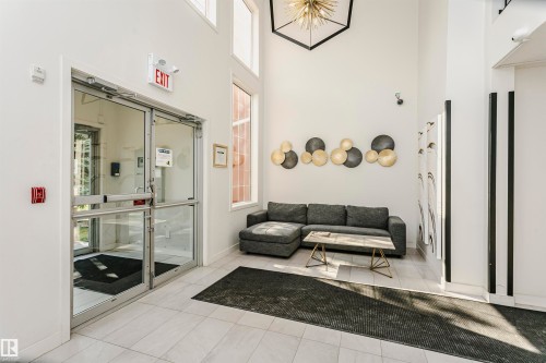 Spacious entry hall featuring double glass doors, high ceilings, large windows, and light-toned tile flooring - #106 12110 106 Av Nw, Edmonton, AB - Indoor Photo Showing Other Room