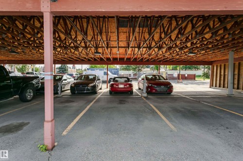 Covered parking structure featuring exposed wooden trusses and paved parking spaces with painted yellow lines - #106 12110 106 Av Nw, Edmonton, AB - Indoor Photo Showing Garage
