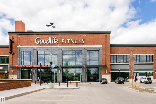 Modern brick and stone commercial building with expansive storefront windows, featuring a prominent entrance and an asphalt parking lot - #106 12110 106 Av Nw, Edmonton, AB - Outdoor