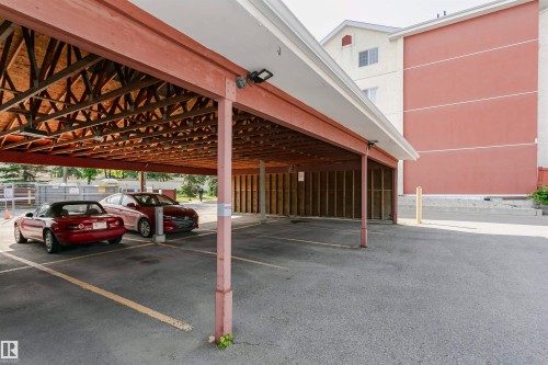 Carport parking featuring an exposed wood beam ceiling, concrete pillars, and asphalt flooring with painted parking lines - #106 12110 106 Av Nw, Edmonton, AB - Outdoor With Exterior