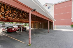 Carport parking featuring an exposed wood beam ceiling, concrete pillars, and asphalt flooring with painted parking lines - 