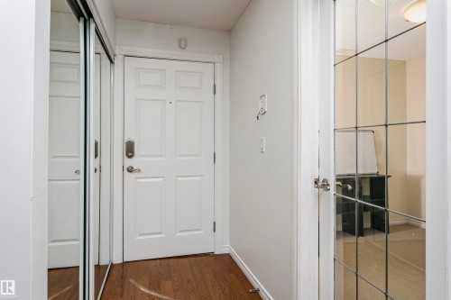 Entryway featuring wood-finish flooring, a white panel door with brushed nickel hardware, and sliding mirrored closet doors - #106 12110 106 Av Nw, Edmonton, AB - Indoor Photo Showing Other Room