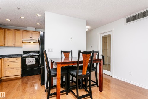 Kitchen and dining area featuring wood-finish flooring, recessed ceiling lighting, light wood cabinetry, dark countertops, and a full-size black refrigerator - #106 12110 106 Av Nw, Edmonton, AB - Indoor
