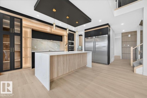 Spacious kitchen featuring a waterfall island with a light wood-finish base, contrasting dark cabinetry, and integrated stainless steel appliances - 427 172 Avenue Nw, Edmonton, AB - Indoor Photo Showing Kitchen