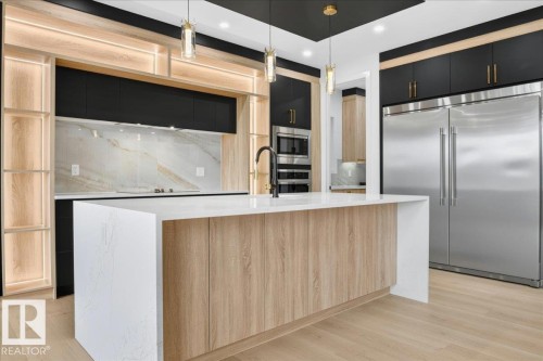 Modern kitchen featuring a large central island with a waterfall countertop, integrated stainless steel appliances, and wood-finish flooring - 427 172 Avenue Nw, Edmonton, AB - Indoor Photo Showing Kitchen With Upgraded Kitchen