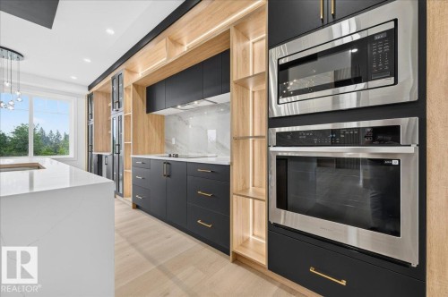 Contemporary kitchen featuring a large white countertop island, dark cabinetry with gold hardware, integrated stainless steel appliances, and wood-finish flooring - 427 172 Avenue Nw, Edmonton, AB - Indoor Photo Showing Kitchen With Upgraded Kitchen