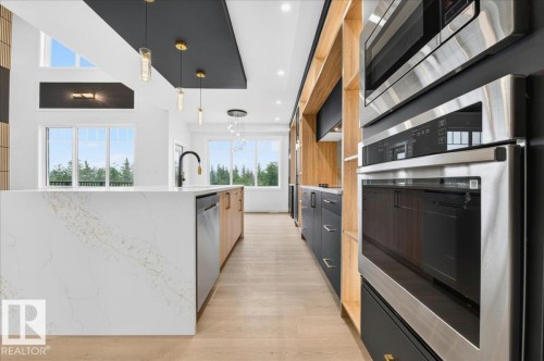 Gourmet kitchen featuring a waterfall island with integrated sink, stainless steel appliances, wood-finish flooring, and high ceilings with recessed and pendant lighting - 427 172 Avenue Nw, Edmonton, AB - Indoor Photo Showing Kitchen With Upgraded Kitchen