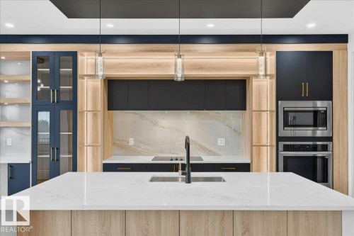 Gourmet kitchen featuring a large island with a waterfall-edge countertop, integrated sink, and matte black faucet - 427 172 Avenue Nw, Edmonton, AB - Indoor Photo Showing Kitchen With Upgraded Kitchen