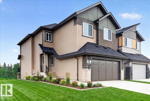 Contemporary duplex exterior featuring a two-car garage, stone accents, and a landscaped front yard with a green lawn - 427 172 Avenue Nw, Edmonton, AB - Outdoor