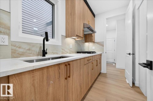 Contemporary kitchen featuring wood-finish cabinetry with brass-tone hardware, a stainless steel undermount sink with a matte black faucet, and a light-toned countertop - 427 172 Avenue Nw, Edmonton, AB - Indoor Photo Showing Kitchen With Double Sink