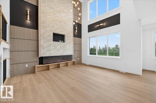 Great room featuring a two-story fireplace with a light-toned stone surround and an integrated electric firebox - 427 172 Avenue Nw, Edmonton, AB - Indoor Photo Showing Other Room