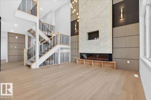 Open-concept living area featuring light wood-finish flooring, a contemporary fireplace with a stone-finish facade, a built-in media niche, and a modern open staircase with metal spindles - 427 172 Avenue Nw, Edmonton, AB - Indoor Photo Showing Other Room