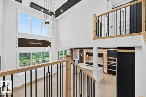 Contemporary open-concept interior featuring a grand two-story window, a dramatic spiral chandelier, and light wood-finish flooring - 427 172 Avenue Nw, Edmonton, AB - Indoor Photo Showing Other Room